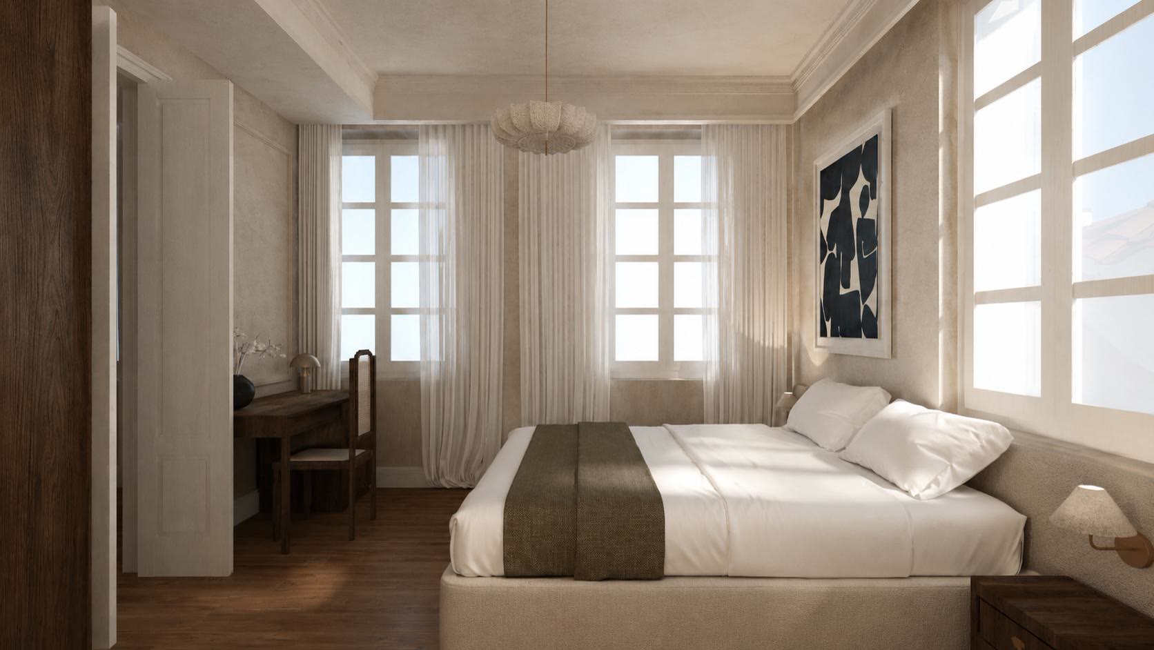 A bright bedroom with two tall windows, sheer curtains, a writing desk with a cane chair and a navy abstract print.